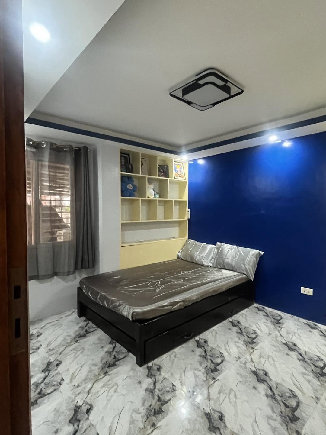 Furnished room with a double bed, built-in shelving and marble-look tiled floor.